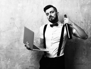 Koyu sakallı ve yüzünde ciddi bir ifade olan adam şişeyi tutuyor.