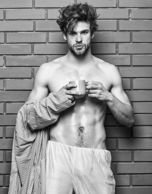 Maço seksi gövde kahve keyfini çıkarın. Atlet uykulu yüz tousled saç giymek bornoz tutun kupa. Sabah kahve kavramı. Sakal içki kahve tuğla duvar arka planı olan adam. Adam tutun çay veya kahve Kupası