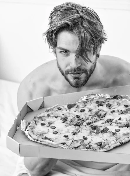 Bir yatağa evde döşeme sırasında tembel kaslı adam yeme pizza portresi. Adam yakışıklı bekar yatakta kahvaltı için peynirli yemek yeme sakallı. Diyet hakkında kimin umurunda. Yatakta pizza yemek.