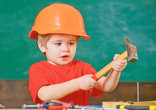 Ragazzo eccitato che gioca con un martello pesante. Carino ragazzo in casco arancione aiutare in officina. Futuro concetto di professione — Foto Stock