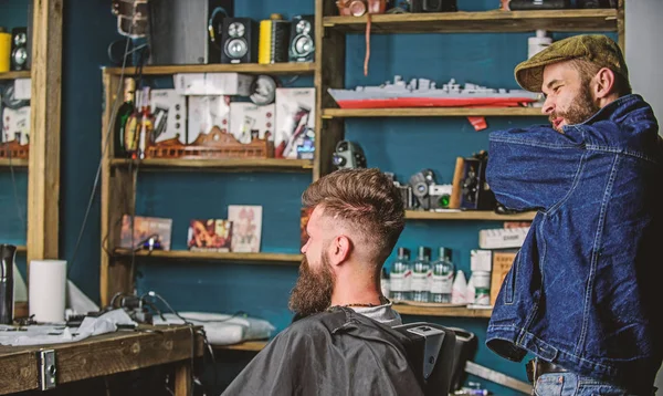 Client and professional master checking result or haircut. Hipster client got new haircut. Haircut concept. Barber finished styling. Barber with bearded man looking at mirror, barbershop background