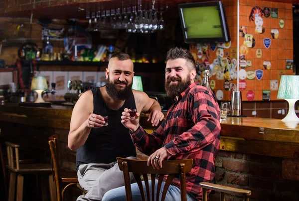 Friday relax in pub. Friends relaxing in pub. Cheers concept. Hipster brutal bearded man drinking alcohol with friend at bar counter. Men drunk relaxing at pub having fun. Strong alcohol drinks