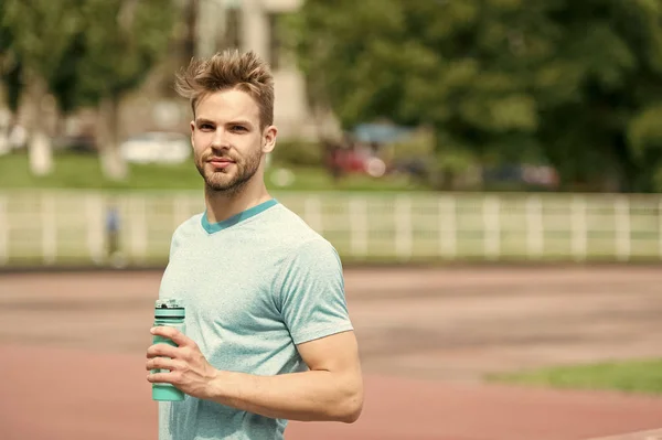 Staying hydrated. Man athletic appearance holds water bottle keep staying hydrated during training. Guy sport clothes refreshing. Athlete cares body hydration after training at stadium sunny day