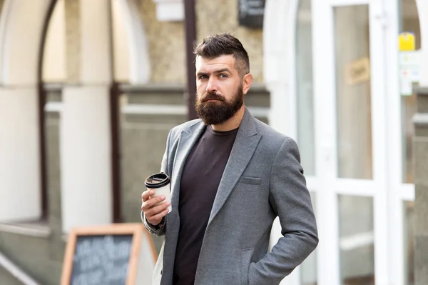 Businessman well groomed appearance enjoy coffee break out of business center. Relax and recharge. Man bearded hipster drinking coffee paper cup. One more sip of coffee. Enjoying coffee on the go