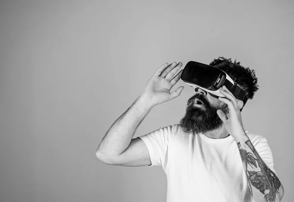 Man with long beard in VR goggles amused with new multidimensional experience. Hipster with trendy beard testing virtual reality headset isolated on blue background. Bearded man checking new gadget