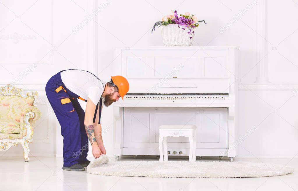Bent worker rolling a carpet. Man with tattoo on arm removing white rug from room. Home renovation concept