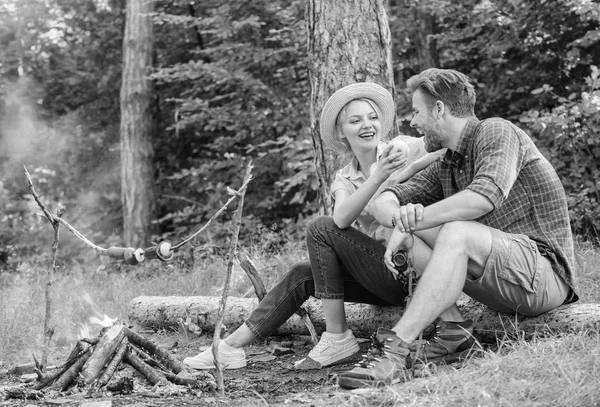 Couple relaxing sit on log having snacks. Family enjoy romantic weekend in nature. Girl offers eat apple while they waiting roasted food. Picnic roasting food over fire. Have snack. Cooking at picnic