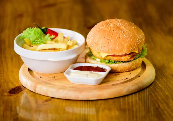 Fast food concept. High calorie snack. Burger menu. Hamburger with sesame seeds and french fries and tomato sauce on wooden board. Delicious burger. Burger with cheese meat and salad. Pub food