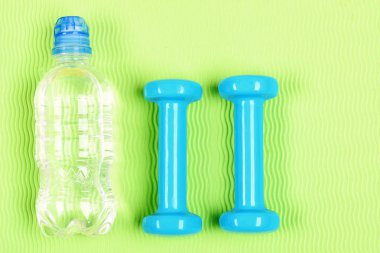 Sağlıklı yaşam ve spor kavram. Çift mavi fitness dumbell ve şişe suyu yeşil zemin üzerine. El ağırlıkları ve su parlak zemin üzerine kümesi. İki plastik dambıl ve açık şişe