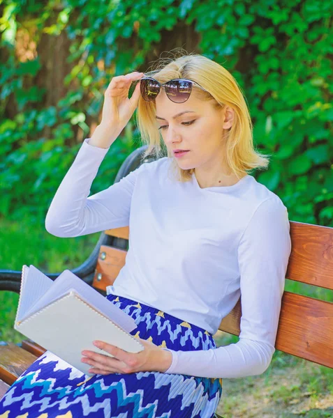 Flickan sitter bänk avslappnande med bokar, grön natur bakgrund. Läsa litteratur som hobby. Tjej sugen på boken Uppehälleläsning. Kvinna blondin tar paus avkopplande i parken läsebok. Ultimata bästa boklistan — Stockfoto