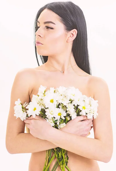 Dziewczyna na spokojny twarz stoi nagi i posiada kwiaty rumianku przed klatką piersiową. Koncepcja zdrowia skóry. Kobieta z gładką i zdrową skórę wygląda atrakcyjnie. Lady obejmuje piersi z kwiatami, na białym tle — Zdjęcie stockowe