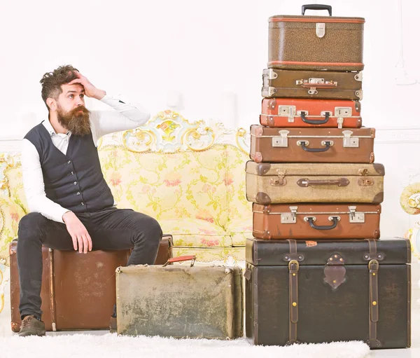 Mann mit Bart und Schnurrbart gepackt Gepäck, weißer Innenraum Hintergrund. Macho elegant auf müdem Gesicht sitzt er, erschöpft am Ende des Packens, neben einem Stapel alter Koffer. Gepäck- und Umzugskonzept — Stockfoto