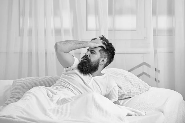 Uomo in camicia sdraiato sul letto sveglio, tenda bianca sullo sfondo. Concetto di sbornia. Macho con la barba e i baffi ha dormito fino a svegliarsi. Ragazzo sul viso deluso doloroso svegliarsi al mattino — Foto Stock