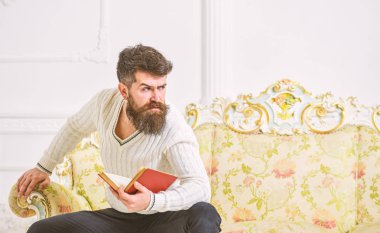 Sakal ve bıyık oturur barok tarzı kanepe, tutar kitap, beyaz duvar arka plan üzerinde olan adam. Maço katı yüz kitap okumayı yeni bitirdim. Adam edebiyat hakkında düşünme. Edebiyat kavramı üzerine düşünceler