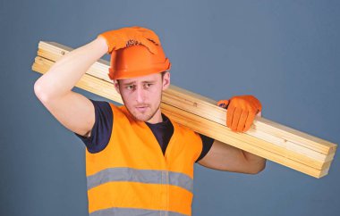 Ahşap malzemeler kavramı. Adam kask, kask ve koruyucu eldiven tutan ahşap kiriş, gri arka plan. Marangoz, woodworker, ciddi bir yüz taşıdığı ahşap kiriş omuz üzerinde güçlü Oluşturucu