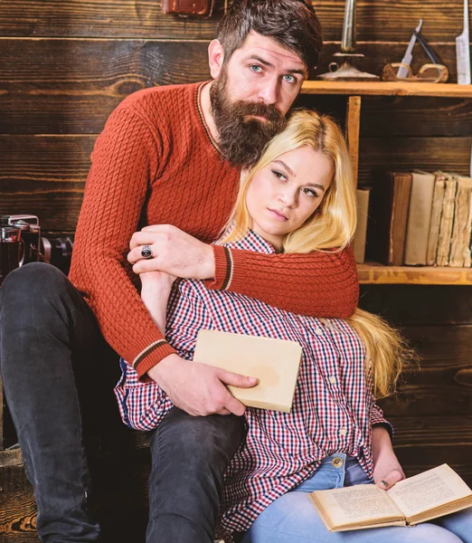 Romantic evening concept. Lady and man with beard on dreamy faces hugs and reading romantic poetry. Couple in wooden vintage interior enjoy poetry. Couple in love reading poetry in warm atmosphere