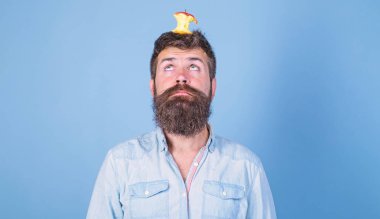 Canlı hedef kavramı. Adam yakışıklı hipster uzun sakal neredeyse kafasına elma güdük hedef olarak yem. Hipster yüz elma güdük hedef üzerinde kafa mavi arka plan, kopya alanı ile şaşırttı. Kilo kaybı gol
