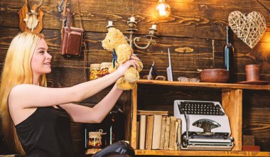 Bayan sarışın oyuncak ayı ile eğlence keyfini çıkarın. Dinlenmek ve rahatlamak kavramı. Kız siyah elbiseli tutar oyuncak ayı oyuncak elinde, ahşap iç arka plan üzerinde. Kadın rüya gibi yüzüne ahşap iç rahatlatıcı