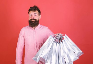 Gülümseyen yüzü üzerinde hipster bağımlısı alışveriş veya Alışverişkoliğin. Satış sezon indirimlerle alışveriş adam. Adam sakal ve bıyık tutan grup alışveriş torbaları, kırmızı arka plan ile. Alışveriş kavramı