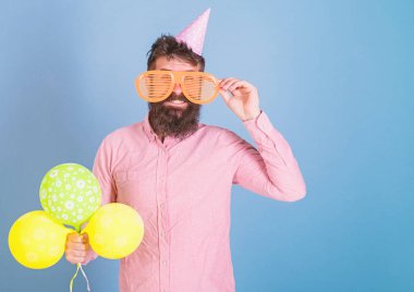 Gülümseyen adam partide, mutluluk kavramı eğleniyor büyük bardaklarda sakallı. Hipster sakal ve bıyık mavi zemin üzerine pembe gömlekli adam. Sanatçı oyuncak balon ile poz Doğum günü şapkalı