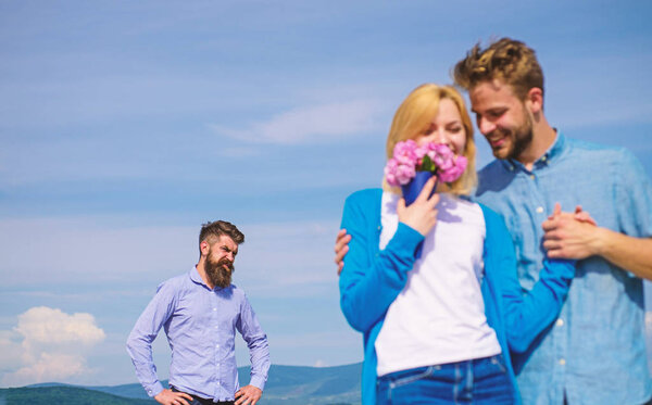 Ex partner watching girl starts happy love relations. New love. Couple in love dating outdoor sunny day, sky background. Couple with flowers bouquet romantic date. Ex husband jealous on background