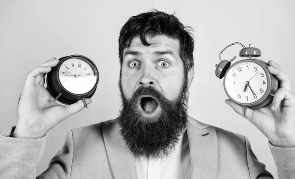 人留胡子的嬉皮士拿着两个不同的钟。这个不折不扣的家伙困惑地面对着时间变化的问题。时区。更改时区会影响运行状况。改变时钟会影响你的健康吗？ — 图库照片