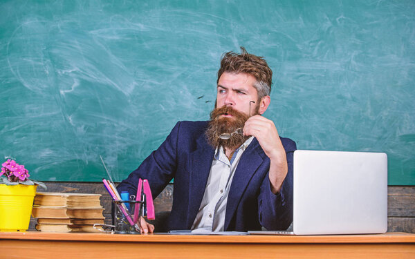 Teacher concentrated bearded mature schoolmaster listening with attention. Teacher formal wear sit table classroom chalkboard background. Teacher listening answer or report. Pay attention to details