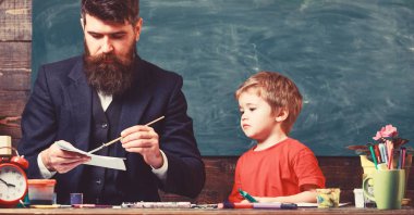 Sanat ders kavramı. Çocuk ve meşgul yüz boyama, resim öğretmeni. Öğretmen sakallı, baba çizim arka plan kara tahta sınıf, küçük oğlu yakınındaki, takılmak iken
