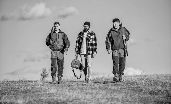 Guys gathered for hunting. Men carry hunting rifles. Hunters with guns walk sunny fall day. Hunting as hobby and leisure. Brutal hobby. Group men hunters or gamekeepers nature background blue sky
