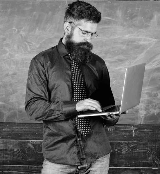 Online-utbildning. Modern teknik utbildning. Hipster lärare bära glasögon och halsduk rymmer bärbar dator. Digital teknik utbildning. Lärare skäggig man med modern laptop chalkboard bakgrund — Stockfoto