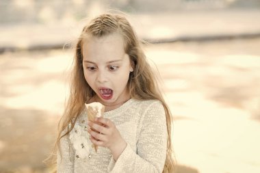Elinde dondurma külahı olan kız çocuğu. Yaz ziyafeti konsepti. Waffle külahında beyaz dondurmalı tatlı düşkünü bir kız. Şok olmuş suratlı tatlı düşkünü kız dondurma yer, hafif arka plan