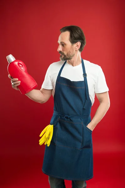 Household laundering. Senior man in apron ready for doing laundry. Mature man holding detergent bottle in hands. Eldery household worker wearing bib apron with rubber gloves. Keeping clothes spotless