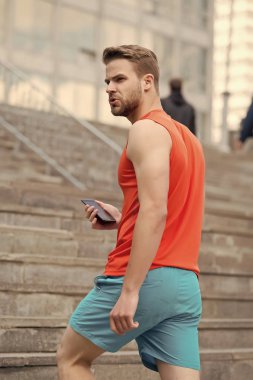 Sakallı adam akıllı telefon, merdiven ile kentsel arka plan ile yürür. Smartphone GPS navigasyon kullanan adam. GPS navigasyon kavramı. Sporcu orienteering Yarışması sırasında gezinti kullanmak