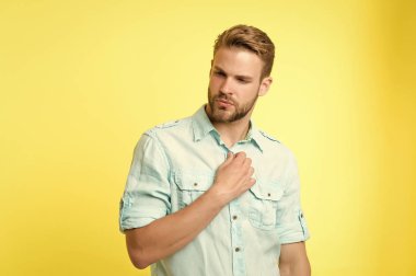 Adam çekici bir keten mavi gömleğe benziyor. Guy Tüylü, sıradan bir tişört. Moda konsepti. Sakin bir adam ciddi bir yüz gömleğin düğmelerini açıyor, sarı arka plan. Elbiselerimi çıkar.