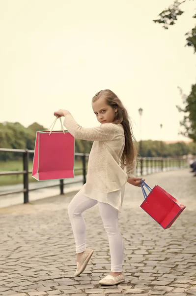 Kid dívka s dlouhými vlasy rádi nakupovat. Módní holka nakupování s růžové tašky. Koncept nákupu. Dívka ráda koupit oblečení. Dívka na klidnou tváří nese nákupní tašky, městské pozadí — Stock fotografie