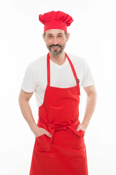 Він чудово готує. Старший кухар з бородою і вусами носить ляльковий фартух. Зрілий головний кухар готує червоний фартух. Бородатий зрілий чоловік в капелюсі шеф-кухаря і фартуха. Домашня кухня — стокове фото