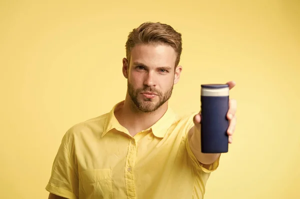 El hombre en la cara segura recomienda champú, fondo amarillo. El tipo con cerdas sostiene una botella de champú, espacio para copiar. El hombre extiende la mano para mostrar la botella de champú. Cuidado del cabello y concepto de champú —  Fotos de Stock