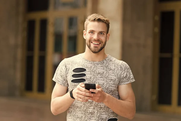 Staying in touch. Send message concept. Man with beard walks with smartphone, urban background. Guy use smartphone to send message stay in touch. Man typing text message smartphone