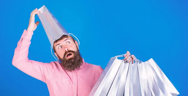 Hombre barbudo con cara retardada y boca abierta con bolsa de papel en la cabeza. Shopaholic volviéndose loco por los altos descuentos, concepto de ventas. Hombre de camisa rosa con barba larga llevando bolsas de compras —  Fotos de Stock