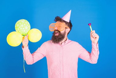 Sakal ve bıyık mutlu yüz tutan hava balonları, mavi arka plan üzerinde olan adam. Parti kavramı. Tatil öznitelikleri ile parti şapkalı adamı kutluyor. Hipster dev gözlük Doğum günü kutluyor