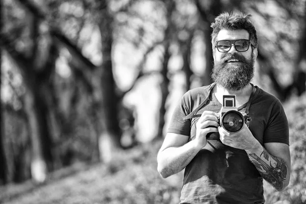 Concepto de fotógrafo. Hombre barbudo hipster fotógrafo mantenga la cámara vintage. Fotógrafo con barba y bigote fotógrafo aficionado fondo de la naturaleza. Hombre con barba larga ocupado con la toma de fotos — Foto de Stock