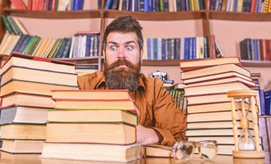 Öğretmen ya da öğrenci sakallı kum saati ve gözlük, defocused ile masaya otur. Kitap kurdu kavramı. Adam şok yüzündeki oturup Kitaplığı'nda, eğitim sırasında kitaplar, kitap rafı adam üzerinde yığınları arasında