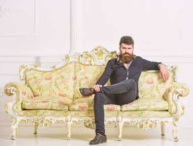 Hipster sıkı yüzünde yalnız oturuyor. Zengin ve yalnız kavramı. Sakallı ve bıyıklı lüks oturma odasında boş zaman harcıyor. Lüks daire sahibi beyaz duvar arka koltukta oturur