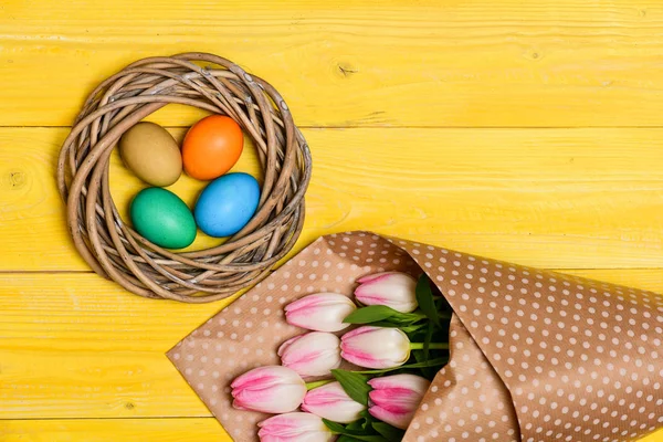 A recolher ovos de Páscoa. Vibrações de primavera. Ovos coloridos e flores de tulipa fresca bouquet no fundo amarelo vista superior. Férias. A tradição celebra a Páscoa. Feliz época de Páscoa. A Páscoa está chegando — Fotografia de Stock