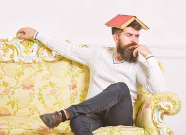 Maço kafasına, çatı gibi açık kitap ile oturuyor. Sıkıcı edebiyat kavramı. Sakal ve bıyık oturur Barok tarzı kanepe, beyaz duvar arka plan üzerinde olan adam. Adam sıkılmış, eski sıkıcı kitap okuma bıkmış