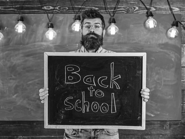 Gymnasialkonzept. Mann mit Bart und Schnurrbart auf ruhigem Gesicht begrüßt die Studenten, Kreidetafel im Hintergrund. Lehrerin mit Brille hält Schultafel mit Titel zurück — Stockfoto