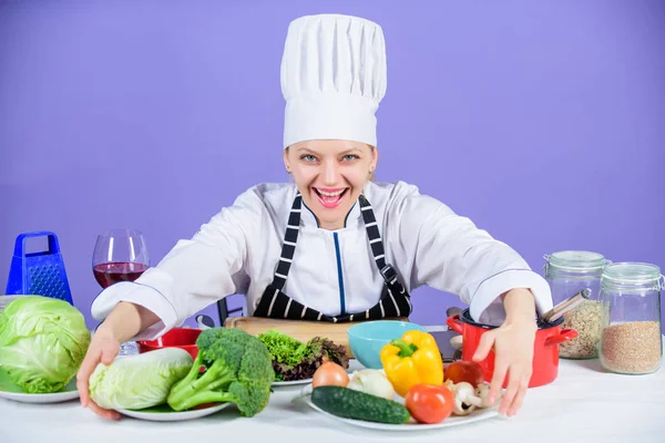 Nainen kokki ruoanlaitto terveellistä ruokaa. Gourmet tärkeimmät astia reseptit. Herkullinen resepti käsite. Tyttö hatussa ja esiliinassa. Terveellistä ruokaa. Tuoreita vihanneksia ainekset ruoanlaittoon aterian. Aloitetaan ruoanlaitto. — kuvapankkivalokuva