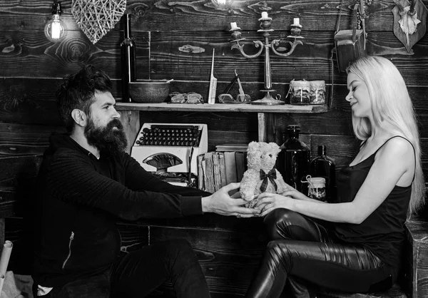 El hombre da a la señora osito de peluche como regalo en el aniversario. Concepto de aniversario. Pareja pasar una velada romántica en la casa de guardabosques, fondo interior de madera. Pareja enamorada en caras sonrientes disfrutar de vacaciones —  Fotos de Stock