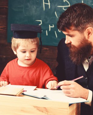 Hevesli çocuk öğretmen ile eğitim. Ödev, çocuk, yardımcı olur kontrol baba evlat. Öğretmen formal giyim ve öğrenci sınıfta kolej, kara tahta arka plan. Evde eğitim kavramı