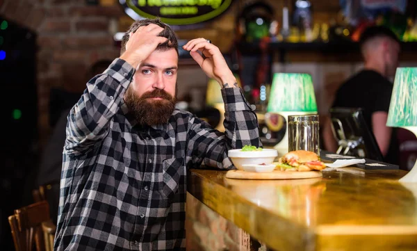 Cheat meal. Delicious burger concept. Enjoy taste of fresh burger. Hipster hungry man eat burger. Brutal hipster bearded man sit at bar counter. Man with beard eat burger menu. High calorie food